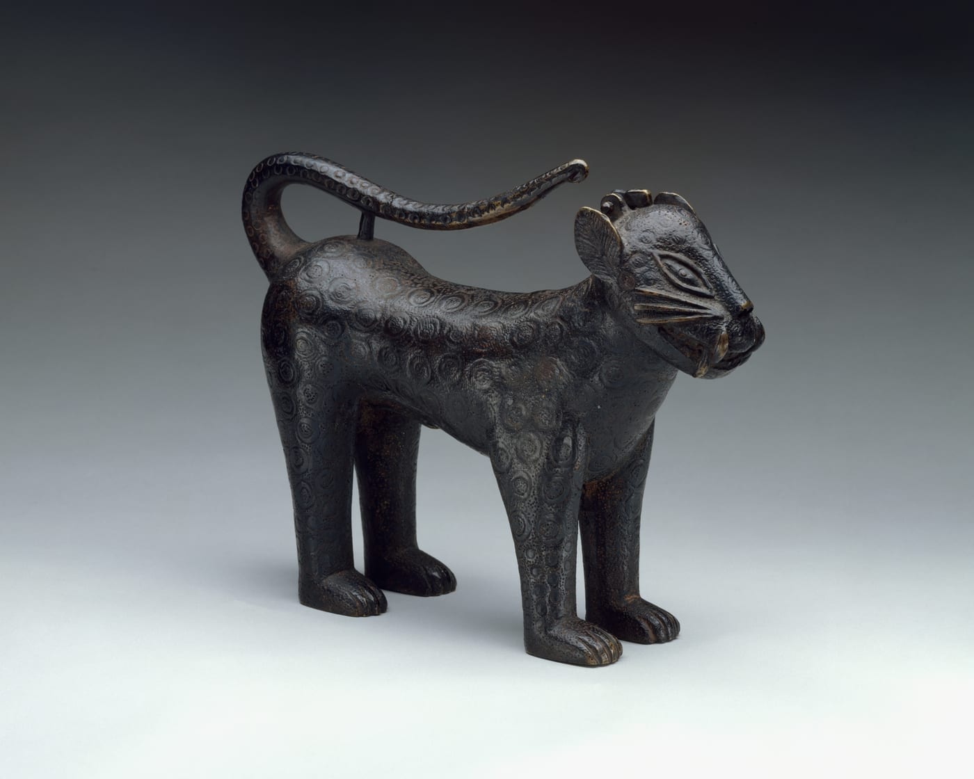 Cast brass vessel in the form of a standing leopard, its body incised with rows of spots, tail curved up over the back, from the Kingdom of Benin.