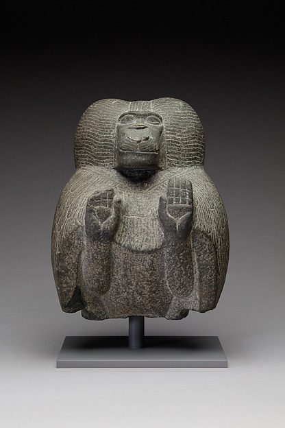 Egyptian stone statuette of a squatting baboon with both hands raised palms outward, carved from dark grey siltstone.