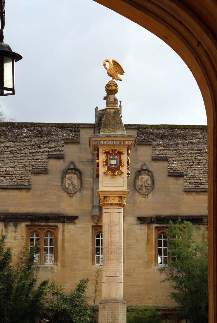 The Pelican Sundial in the front quadrangle of Corpus Christi College, Oxford: a tall stone pillar carrying multiple dial faces and coats of arms, topped by a gilded pelican standing on a golden sphere, seen through a stone archway.
