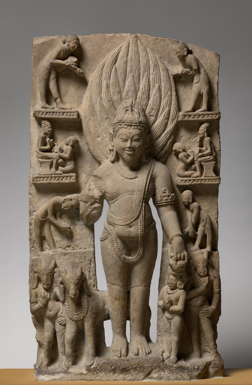 Sandstone stele of Agni, god of fire, standing with flame-like hair and a beard, surrounded by small carved figures, with a garlanded ram standing in profile in the base register at his feet.