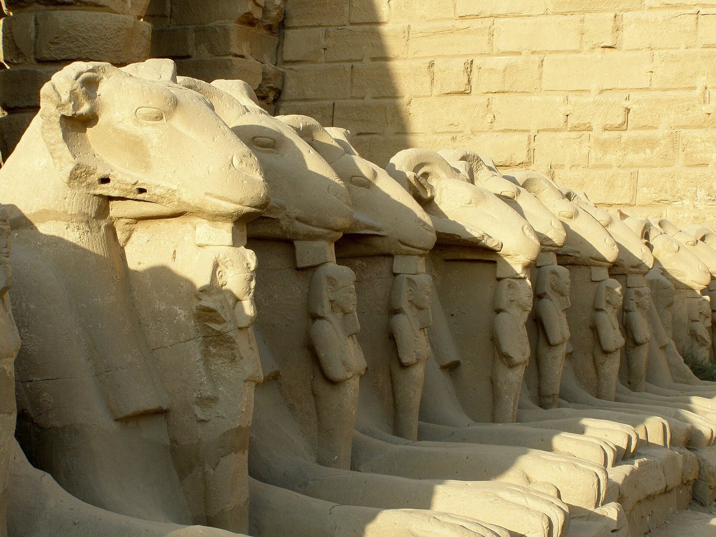 A row of stone ram-headed sphinxes with curled horns lining a wall in the great court of the temple of Amun-Ra at Karnak, Luxor.